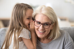 Cute Little Granddaughter Whispering In Ear Telling Secret To Grandma