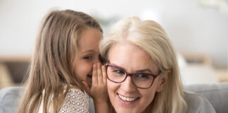 Cute Little Granddaughter Whispering In Ear Telling Secret To Grandma