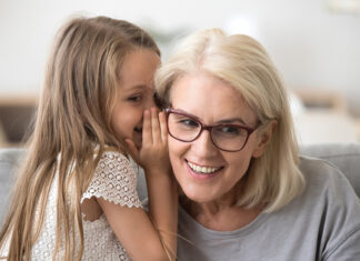 Cute Little Granddaughter Whispering In Ear Telling Secret To Grandma