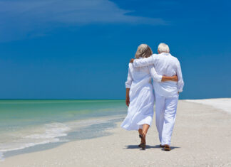 Rear View Of Senior Couple Walking On Beach