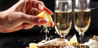 Prosecco Bar Concept. Open Oysters Lie On Crushed Ice With Lemon And Lime, Next To A Glass Of Champagne. Background Image. Copy Space.