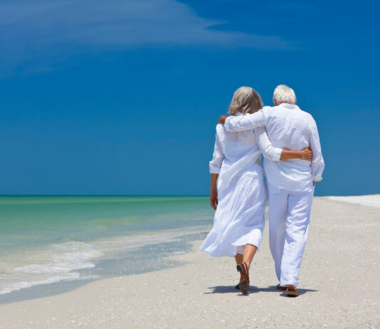 Rear View Of Senior Couple Walking On Beach
