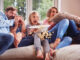Frightened Family Sitting On Sofa At Home Watching Horror Movie On Tv With Popcorn