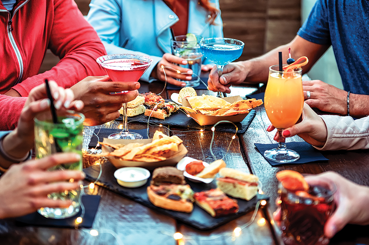 Group Of Friends Enjoying Appetizer Drinking And Eating In A Bar Close Up Of Hands Of Young People Holding Colorful Cocktails In The Happy Hour Time Social Gathering Party Time Concept