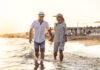 A Middle Aged Couple Walking Hand In Hand On The Beach At Sunset.