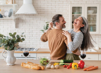 Happy Cheerful Middle Aged Mature Couple Family Parents Dancing Together In The Kitchen, Preparing Cooking Food Meal For Romantic Dinner, Spending Time Together. Active Seniors