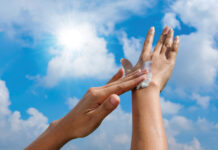 A Woman Is Applying Sunscreen And Skin Care To Protect Her Skin From Uv Rays. She Is Applying Sunscreen On Her Hands And Arms. The Sun Symbol Is A Very Sunny Background. Health And Skin Care Concept