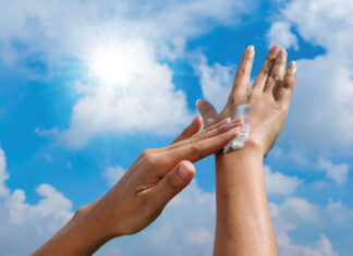 A Woman Is Applying Sunscreen And Skin Care To Protect Her Skin From Uv Rays. She Is Applying Sunscreen On Her Hands And Arms. The Sun Symbol Is A Very Sunny Background. Health And Skin Care Concept